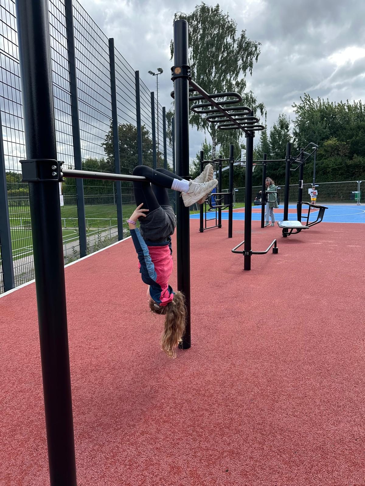 Ein Kind hängt kopfüber an einer Stange der Calisthenics-Anlage
